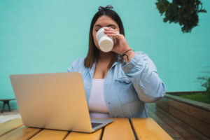 Photo of a woman in the Orlando, FL area on a computer drinking a coffee representing someone logging in for online therapy in Florida.