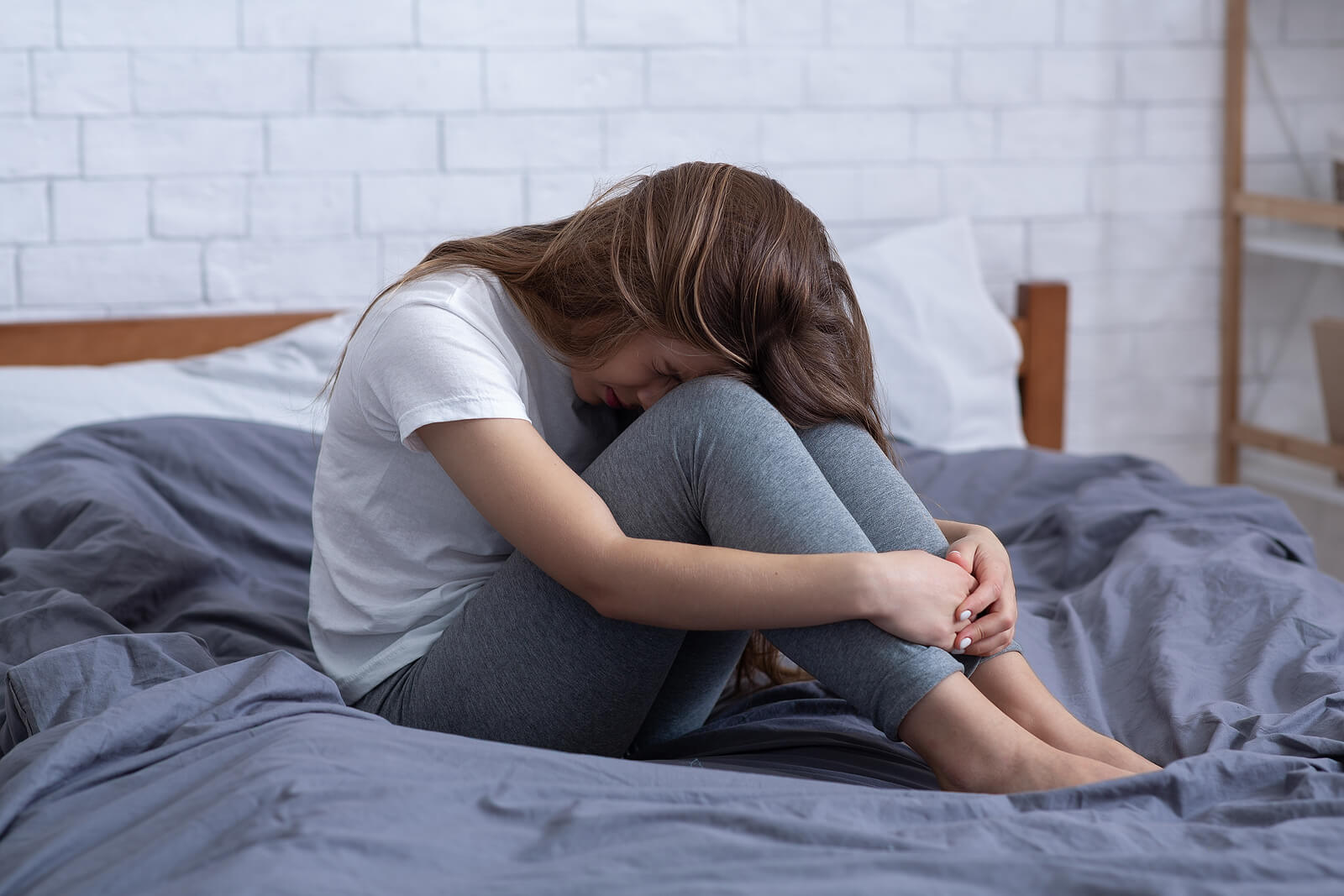 Image of a young adult sitting on a bed looking upset with can be a sign of depression in teens in Orlando, FL.