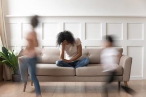 Image of a woman sitting on a couch upset while her kids run around. Being overwhelmed like this is a common for those suffering from depression symptoms in Orlando, FL. If this is something you struggle with it is time to seek depression treatment. Whether you are in Orlando or Winter Park, FL depression therapy can give you the coping skills and support to feel better.